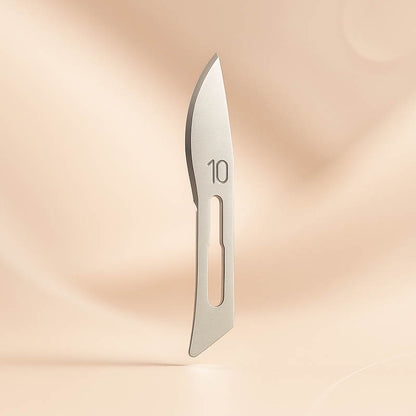 Luxury #10 surgical dermaplaning blade displayed on a soft blush background — precision stainless steel design engraved with “10,” ideal for estheticians seeking professional, high-quality tools for safe and effective exfoliation treatments.