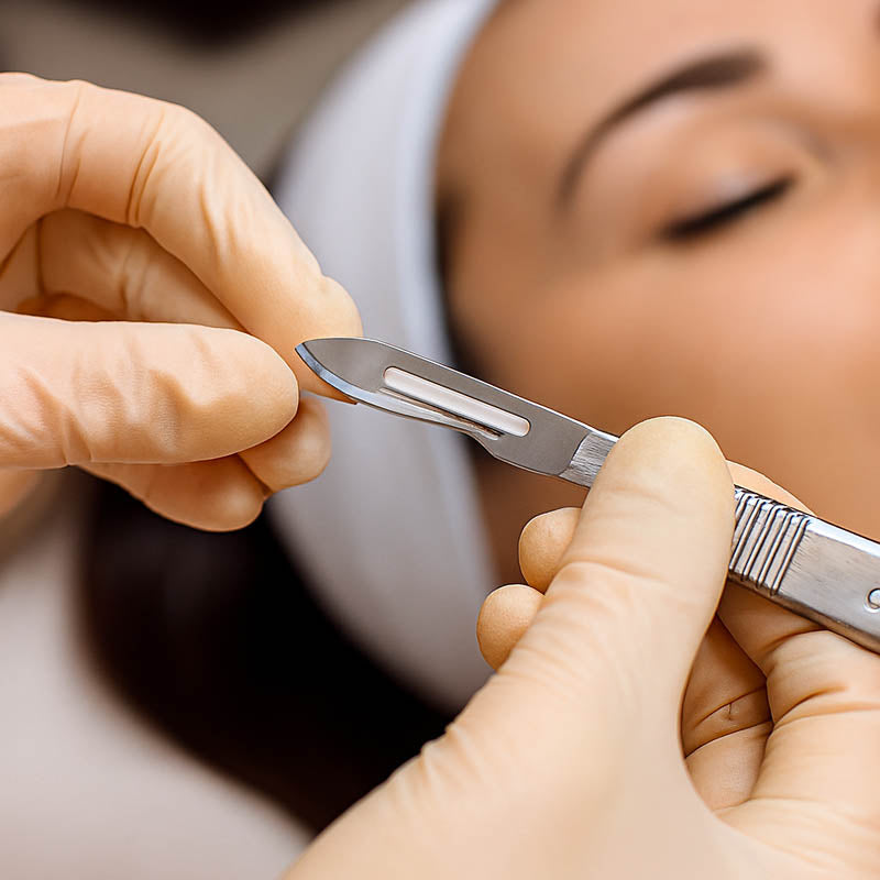 Professional esthetician attaching a #10 dermaplaning blade to a stainless steel handle using proper technique — showcasing safety, precision, and professional skincare preparation in a clean, spa-like treatment environment.