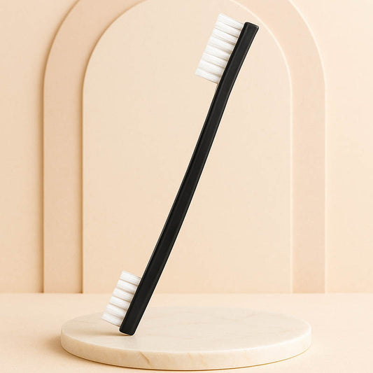 Professional black double-ended instrument cleaning brush with white bristles displayed on a beige marble spa surface under soft lighting, luxury minimalist background designed for esthetician