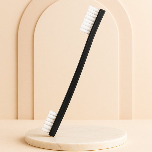 Professional black double-ended instrument cleaning brush with white bristles displayed on a beige marble spa surface under soft lighting, luxury minimalist background designed for esthetician